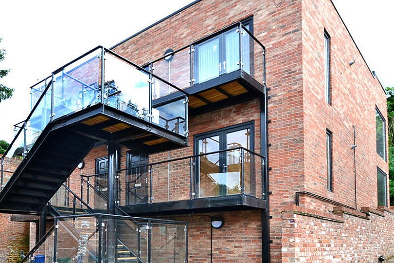 Svart balkongdörr i en tre våningar byggnad med en glaserad balkong